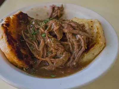 A bowl of food with meat and sauce on top.