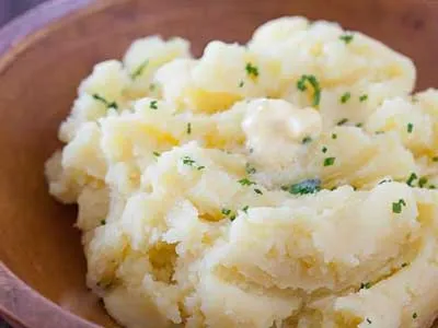 A bowl of mashed potatoes with parsley on top.