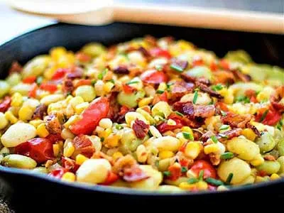 A pan of corn and bacon with tomatoes.