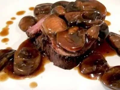 A plate of steak and mushrooms with sauce.