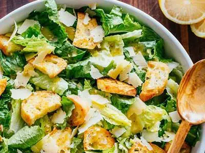 A bowl of salad with lettuce, croutons and parmesan cheese.