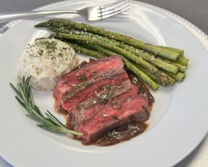 A plate of food with asparagus, rice and steak.